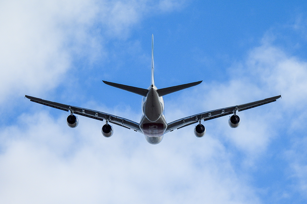 Airplane seen from behind and below flying through slightly cloudy blue skies