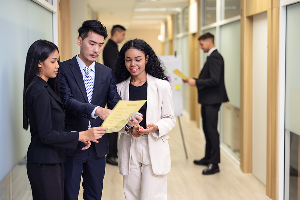 a group of professionally dressed people consulting a document while standing in a hallway